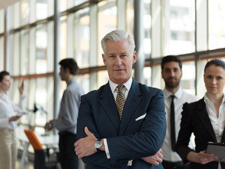 portrait of senior businessman as leader  with staff in backgrou