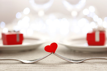 Heart between two forks on a table set for two, close up