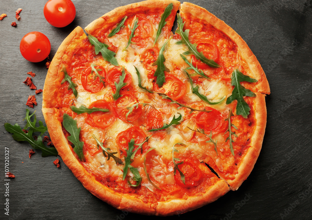 Margherita pizza with tomatoes and arugula on slate plate