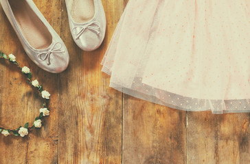 vintage chiffon girl's dress, floral tiara next to ballet shoes on wooden background. vintage filtered image
