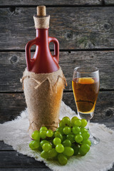 Wineglass of white wine, bottle of wine and grapes on a wooden background