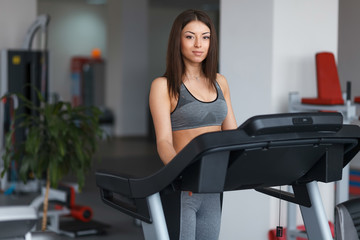 Beautiful young girl engaged in fitness in the gym. He runs on the treadmill. Performs physical exercise.