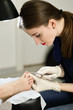 Manicurist working with forceps and make a girl pedicure. Portrait profile of manicure in white gloves.