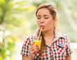 © Fotos 593 - Young woman in square pattern shirt enjoying a yellow juice with eyes closed, garden environment