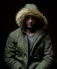 Low key studio portrait of suspicious young adult caucasian model wearing winter coat with hood on. Isolated on black.