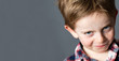 closeup portrait of a young mischievous child with freckles teasing and grumbling with fun look and joke, copy space on grey background studio