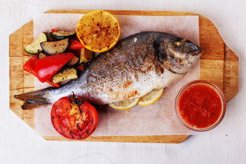 white fish dorado whole vegetables, corn, tomato lemon pepper board isolated background seabass