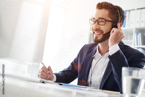 Fotografia Smiling businessman using headset when talking to customer