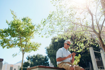 Wall Mural - Senior man sitting outdoors and using cell phone