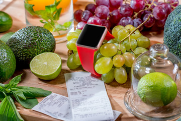 Wall Mural - Smart watch with empty screen lying with green fruits and receipts on the table. Smart watch payment technology 