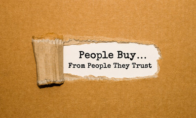 The text People buy from people they trust appearing behind torn brown paper