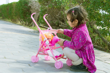 Little girl plays with her doll in a stroller - outdoors portrait
