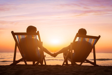 Wall Mural - romantic love background, honeymoon, couple relaxing on the beach at sunset