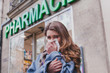 © Song_about_summer - sick cold woman next to a pharmacy, flu concept, buy medicaments