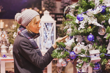 people at christmas market, woman choosing festive decoration in the shop