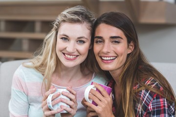 Wall Mural - Two beautiful women sitting side by side with a mug of coffee