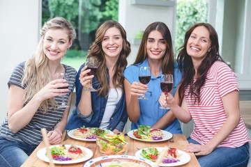 Wall Mural - Friends holding glass of red wine while having meal