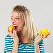 natural vitamins concept - hungry young blond woman with appetite for orange versus lemon held in both hands, studio shot