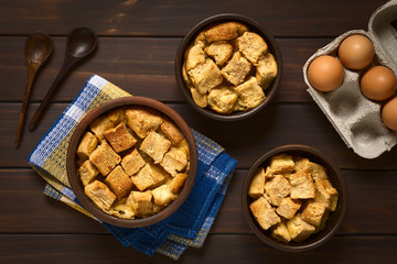 Wall Mural - Bread pudding made of diced stale bread, milk, egg, cinnamon, sugar and butter, photographed on dark wood with natural light