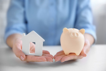 Sticker - Savings concept. Woman holding piggy bank in one hand and house figure in another, close up