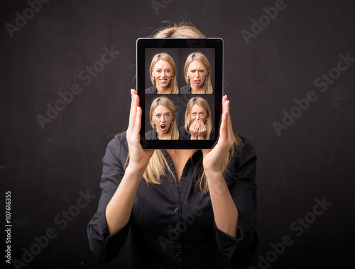 Fotografie, Tablou Woman holding tablet with different faces in front of her