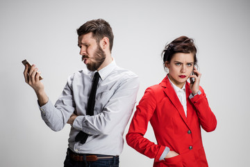 Business concept. The two young colleagues holding mobile phones on gray background