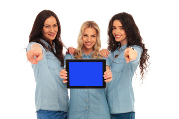 Poster - three happy  women presenting tablet's screen and pointing the f