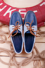 Blue Boat shoes with orange laces near rope on light wood background close up