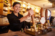 A young woman working behind a bar looking to camera, horizontal