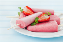 Homemade strawberry ice cream or popsicles in plate on blue wooden table, frozen fruit juice, selective focus