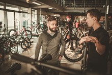 Salesman Showing A New Bicycle To Interested Customer In Bike Shop.