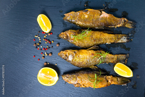 Fotografija top view of fried tench fish served with aromatic rosemary, lemon and dry pepper