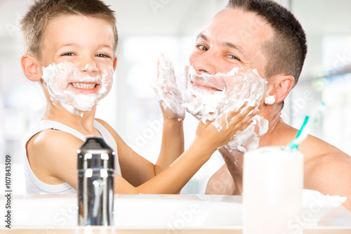 Fotografija  happy child have fun with dad with shaving foam in the bathroom