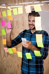 Wall Mural - Man using mobile phone while writing on sticky notes 