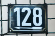Weathered grunge square metal enameled plate of number of street address with number 128 closeup