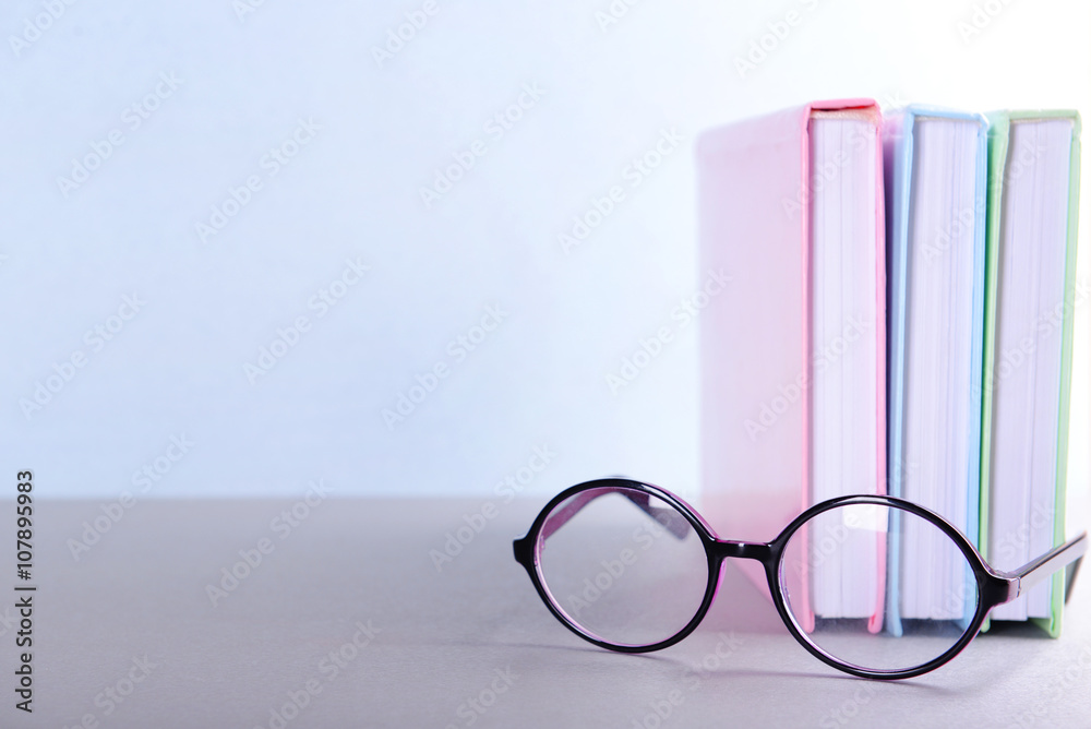 Books and eyeglasses on grey table against blue wall