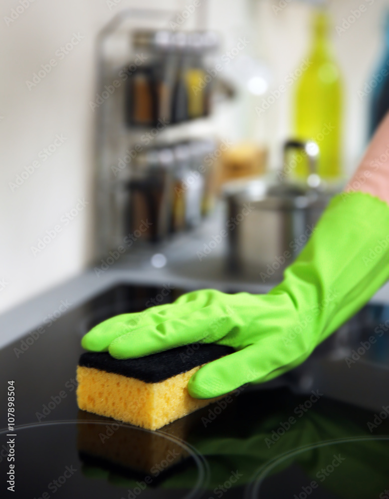 Human hand in protective gloves washing electric hob in the kitchen