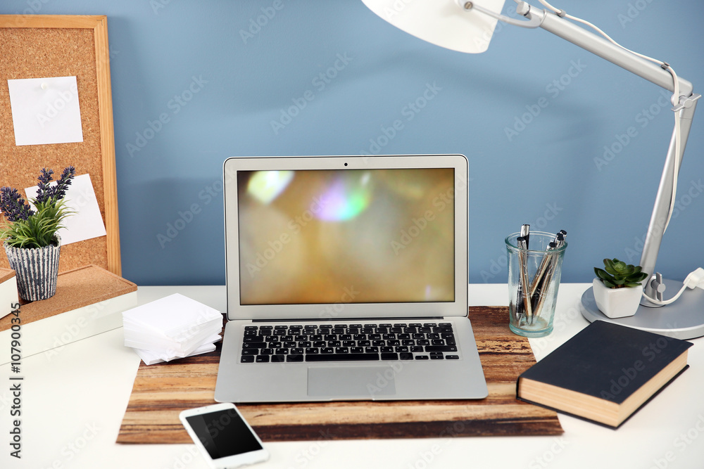 Workplace with laptop, mobile phone and table on blue wall background