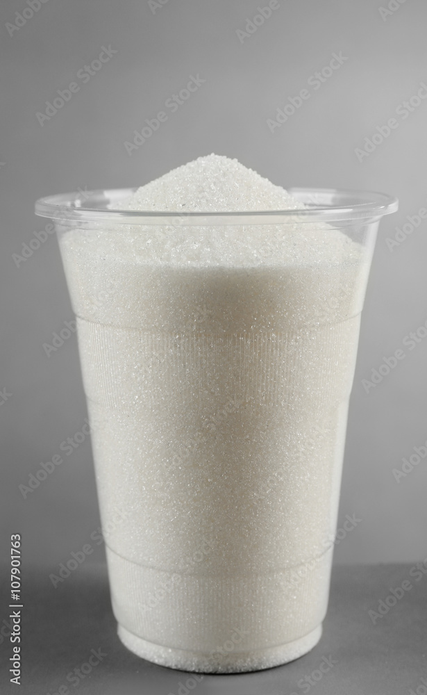 Plastic glass full of sugar on grey background