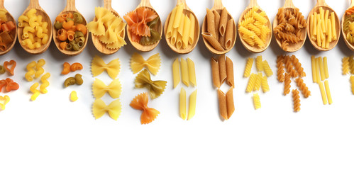 Different types of dry pasta in wooden spoons on white background