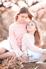 Wall Mural - Two smiling sisters sitting in meadow outdoors. Looking to each other. Togetherness 