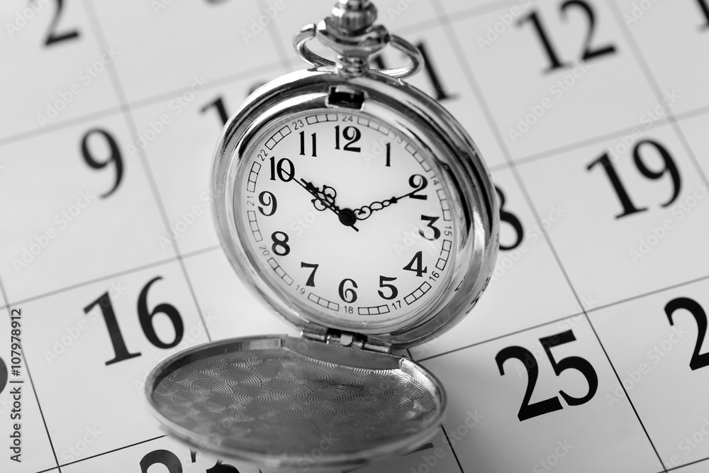 Vintage silver pocket watch laying on calender page with dates, close up
