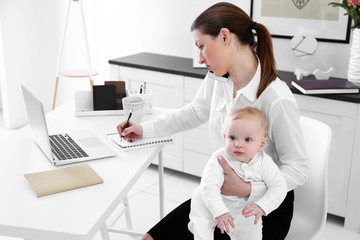 Wall Mural - Businesswoman with baby boy working from home using laptop and mobile phone