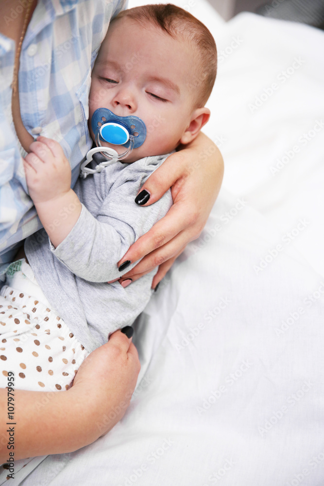 Loving baby with dummy sleeping in mother's hands, close up