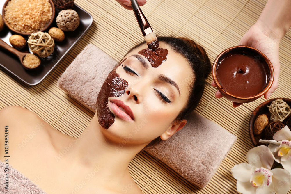 Beautiful young girl getting chocolate mask in spa salon