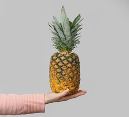 Poster - Female hand holding whole pineapple on grey background