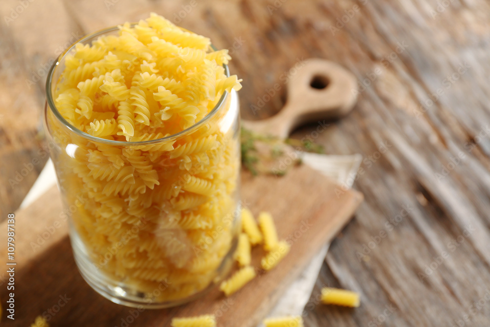 Raw pasta in glass jar on wooden background