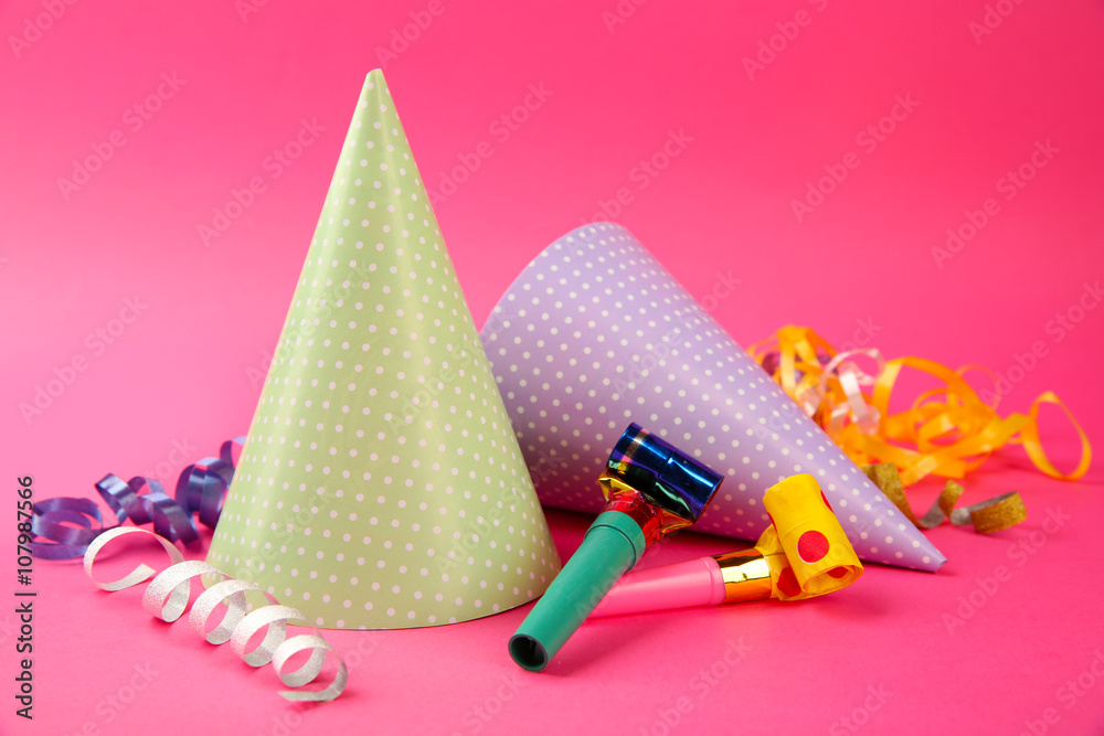 Two dotted Birthday hats with serpentine streamer and noise makers on pink background