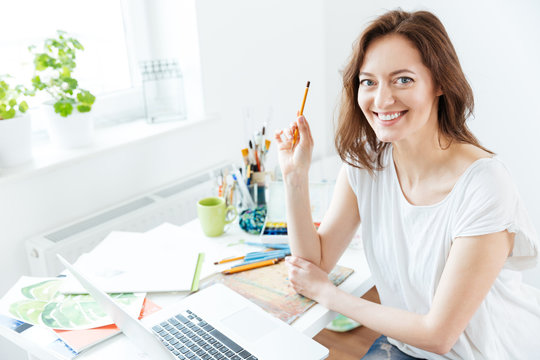 Happy pretty woman artist using laptop in art studio