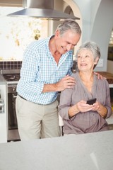 Wall Mural - Happy senior man standing besides wife sitting in kitchen